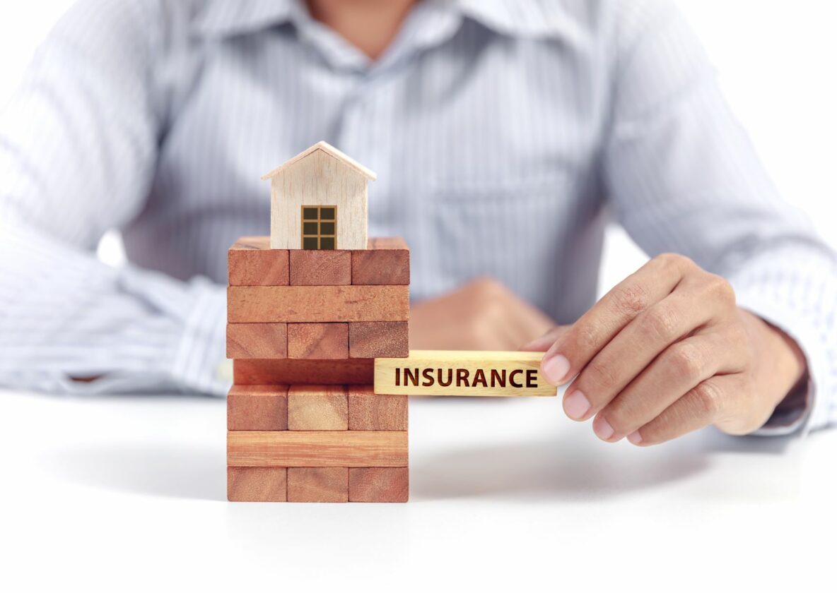 man pulling out Jenga piece with insurance on it in a stack that has a small house at the top