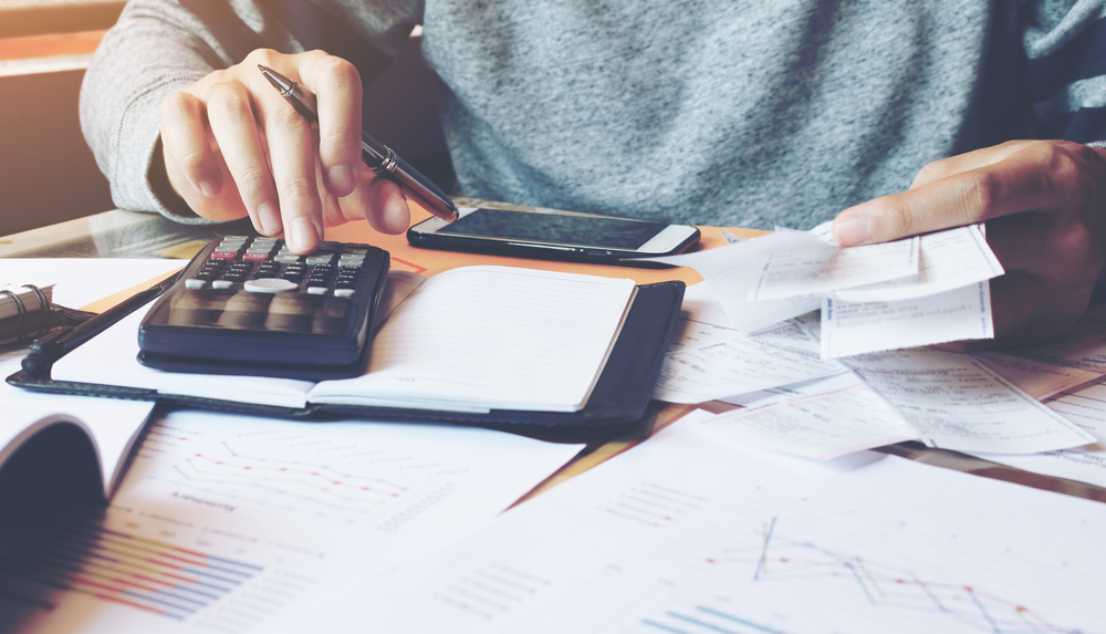 man using calculator with papers scattered around him