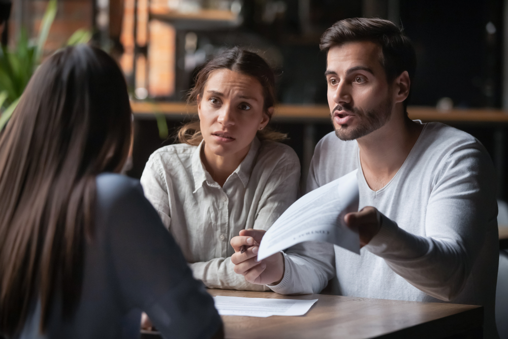 woman and man (has paper in hand) with worried expression looking at woman across for them